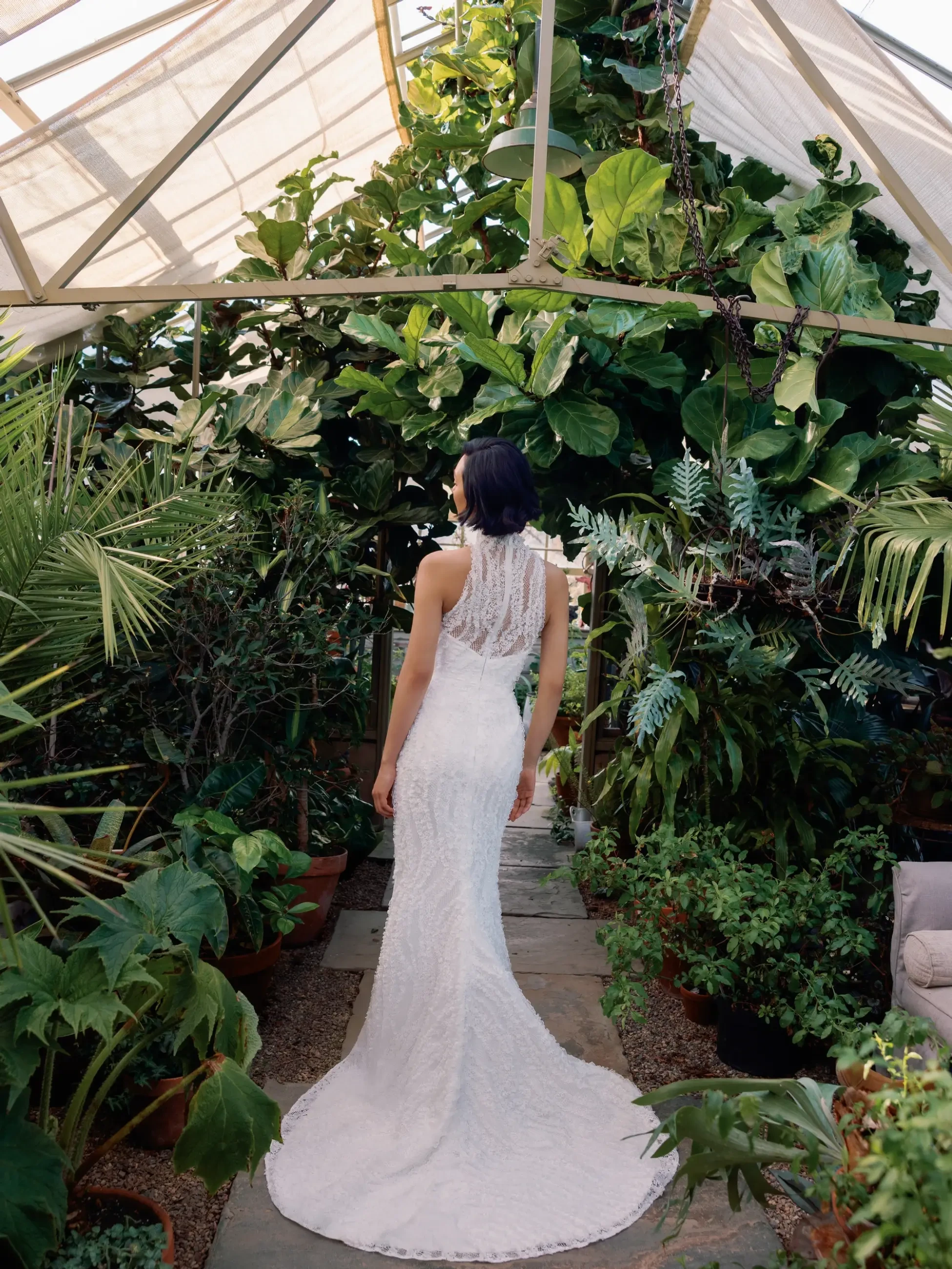 Model is wearing a slim flare gown detailed with three-dimensional embroidered lace, a chic halter neckline, and a graceful chapel-length train.