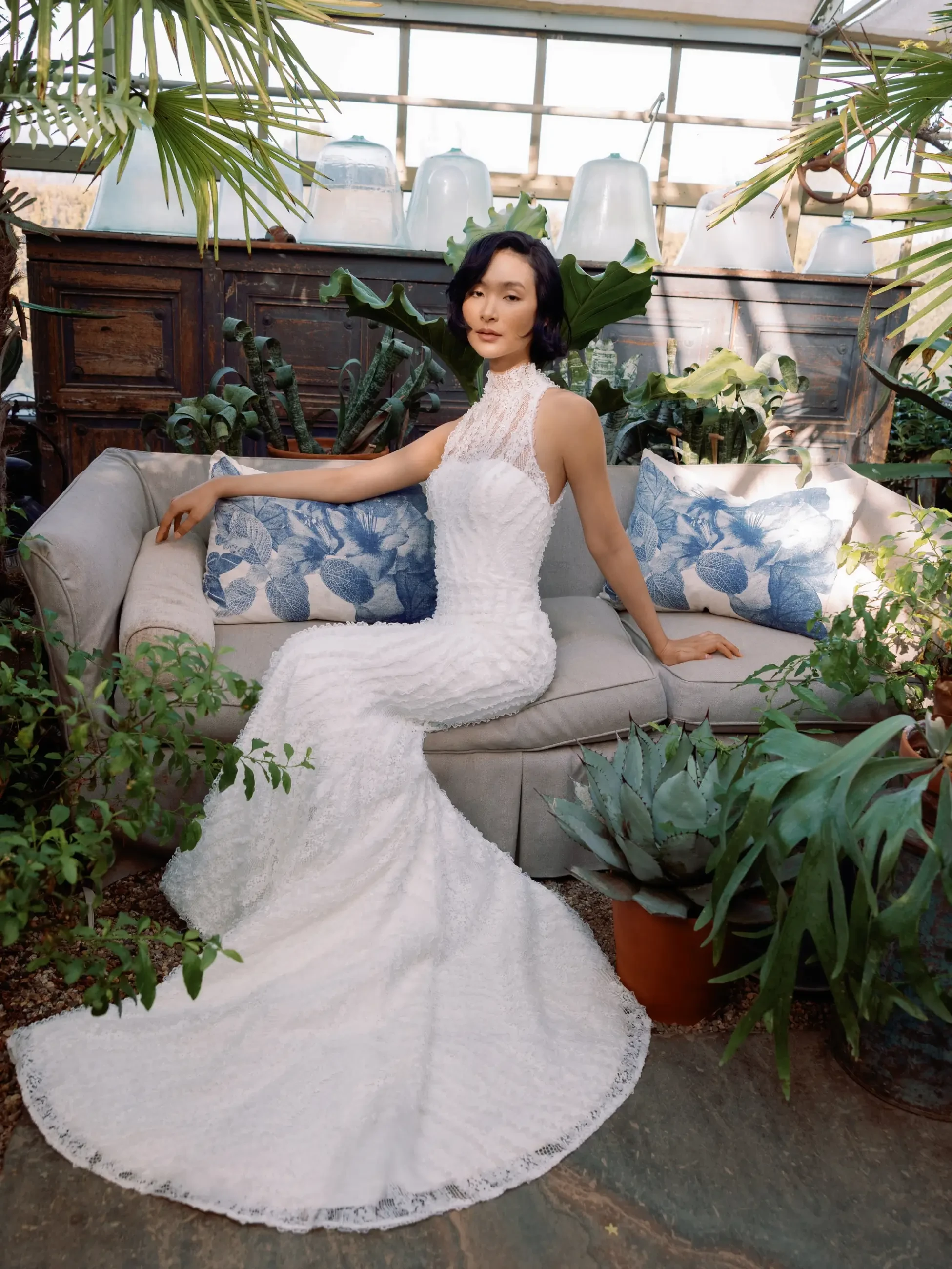 Model is wearing a slim flare gown detailed with three-dimensional embroidered lace, a chic halter neckline, and a graceful chapel-length train.