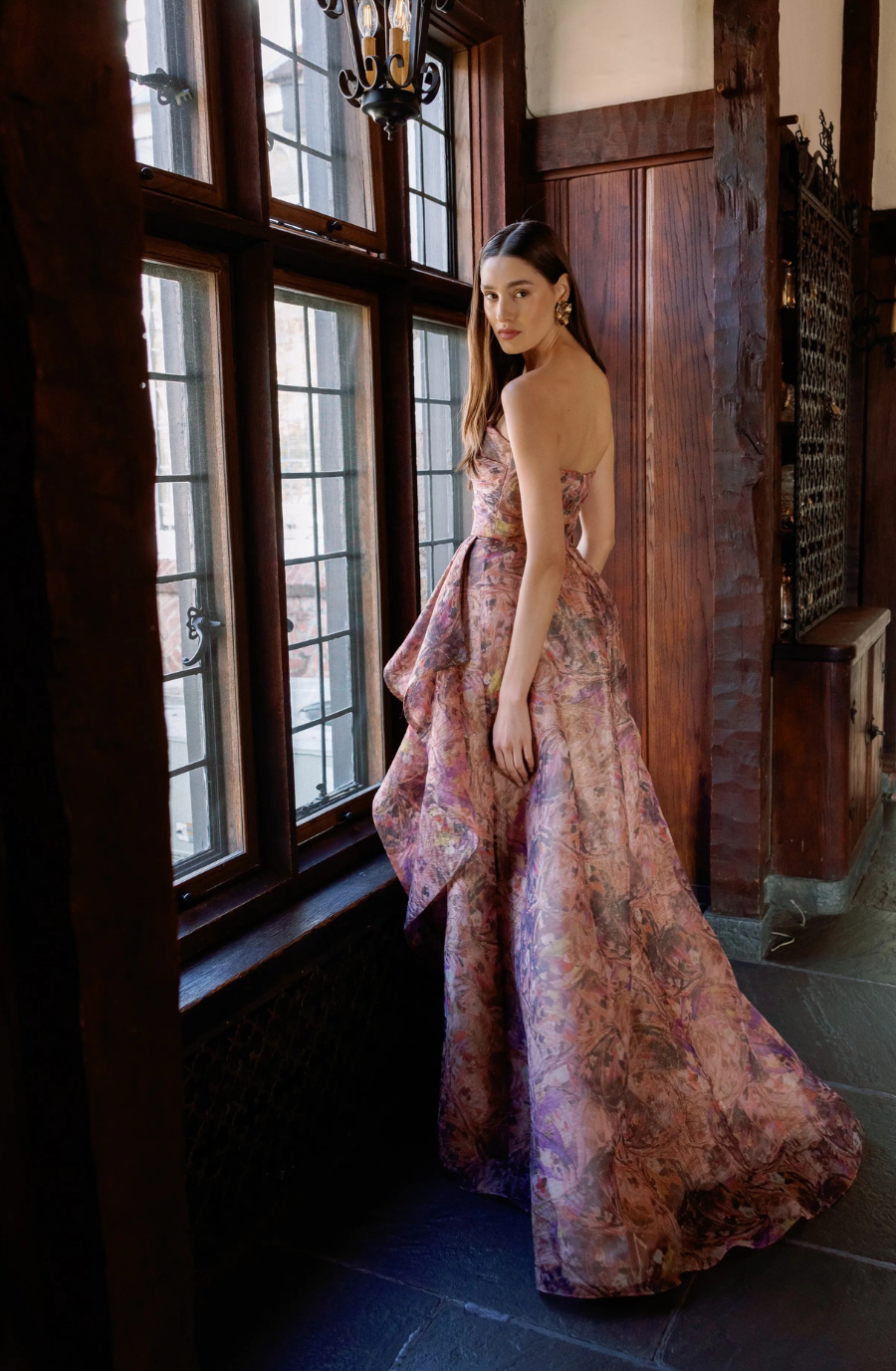 Model is wearing a strapless floral gown with a sweetheart neckline, hand-draped bodice, slim skirt, and high slit.