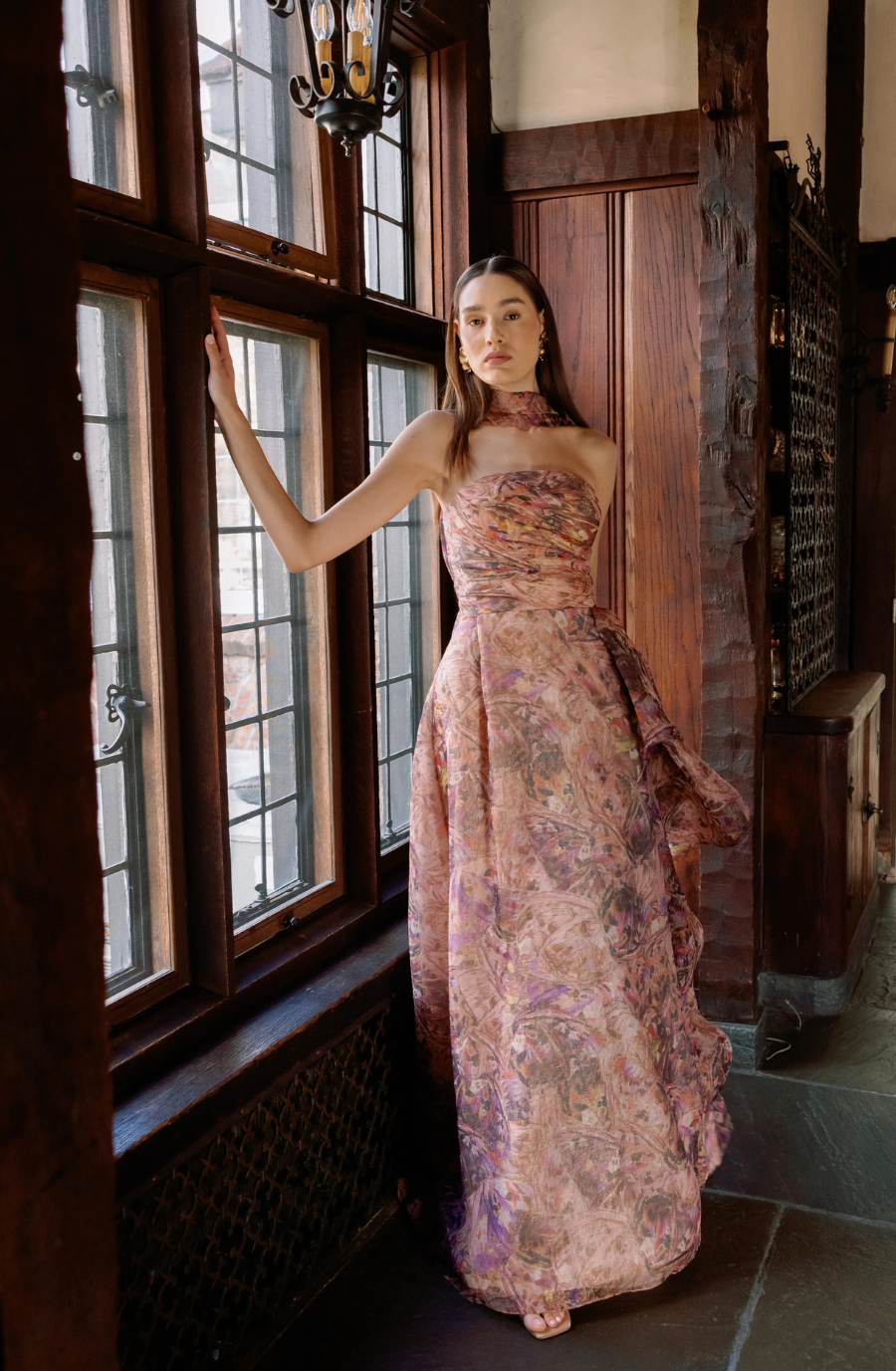 Model is wearing a strapless floral gown with a sweetheart neckline, hand-draped bodice, slim skirt, and high slit.
