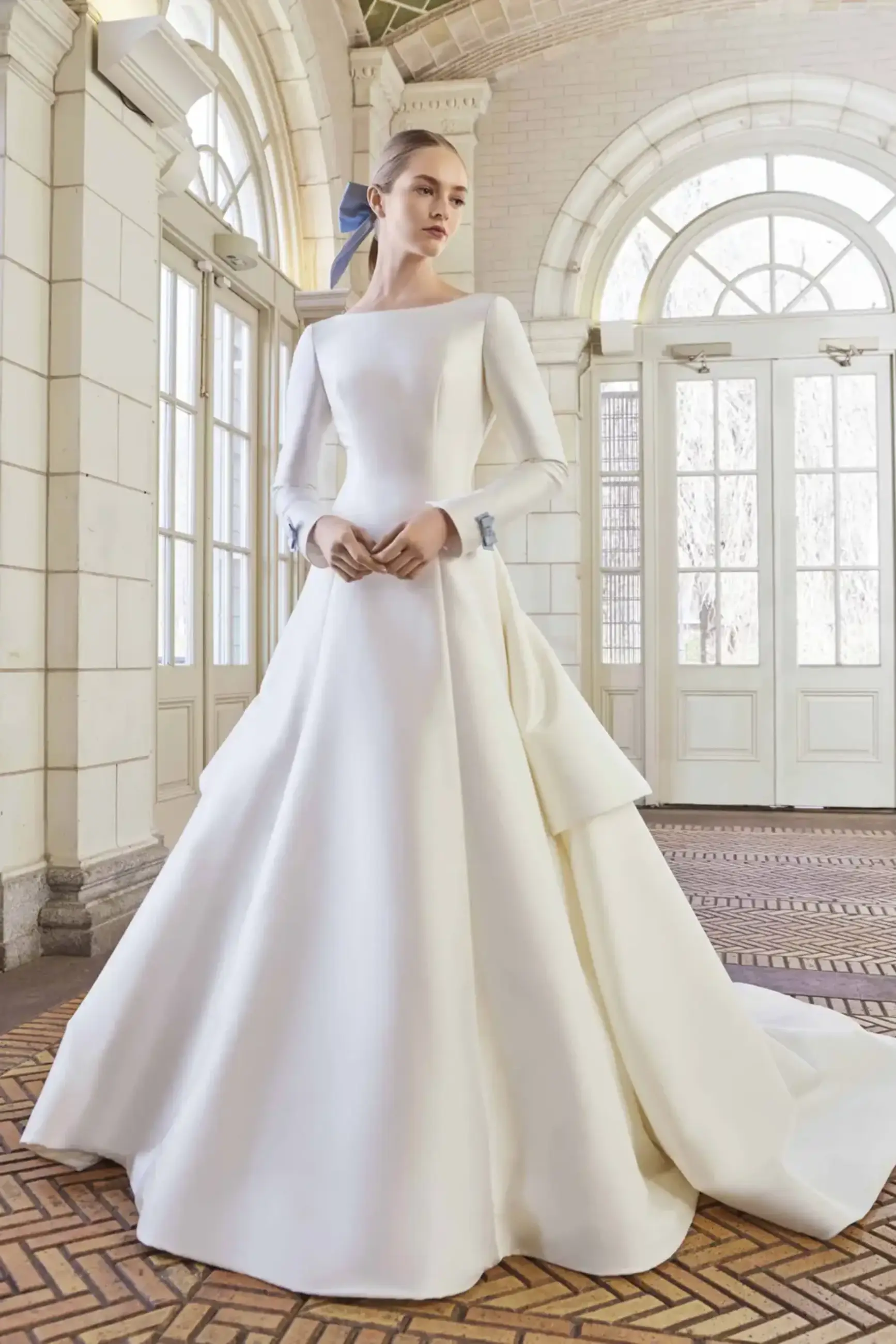 model is wearing a long sleeve open back wedding dress with little blue bows on the back