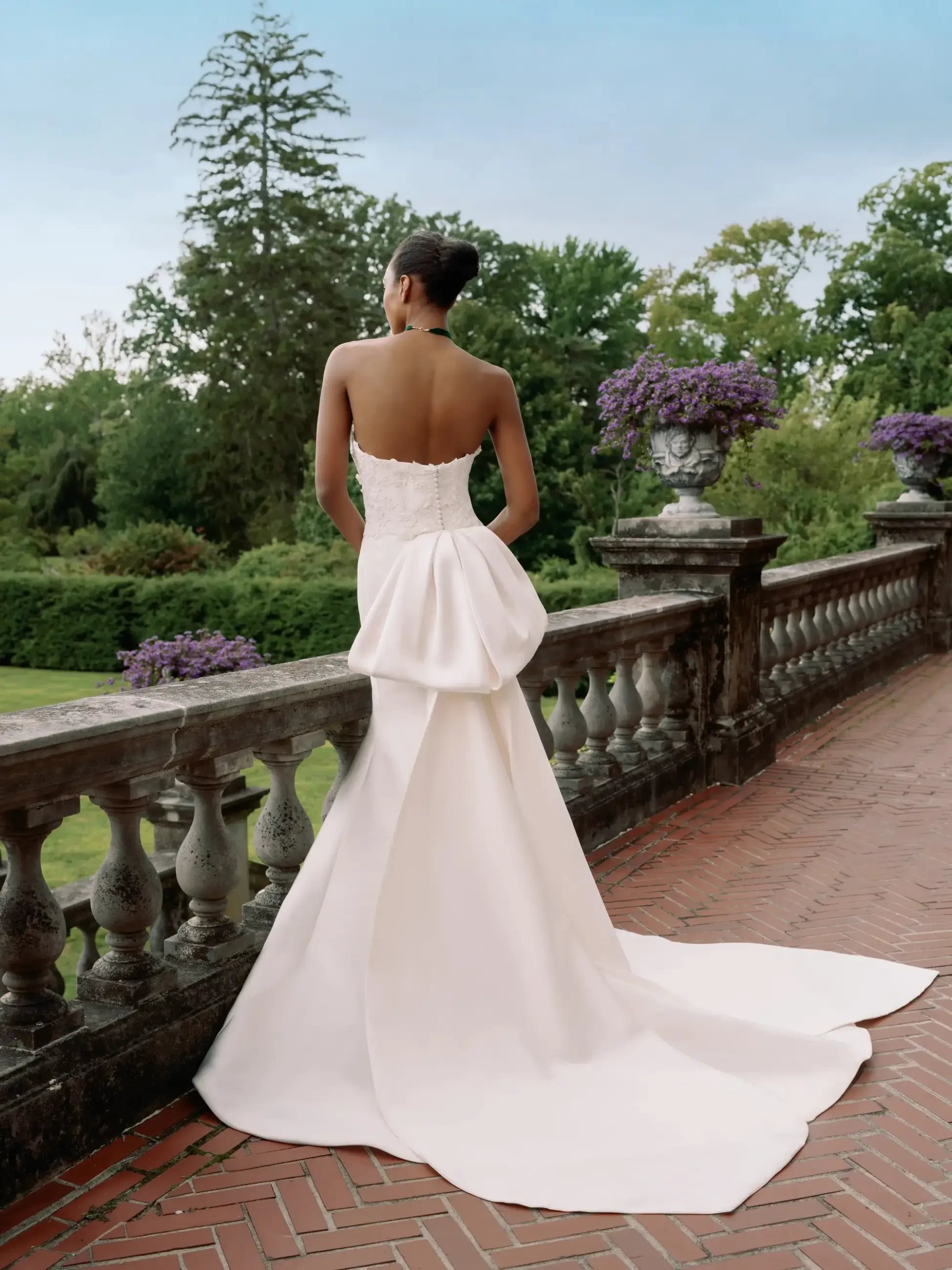 Model is wearing a slim flare strapless wedding dress with a large bow on the back