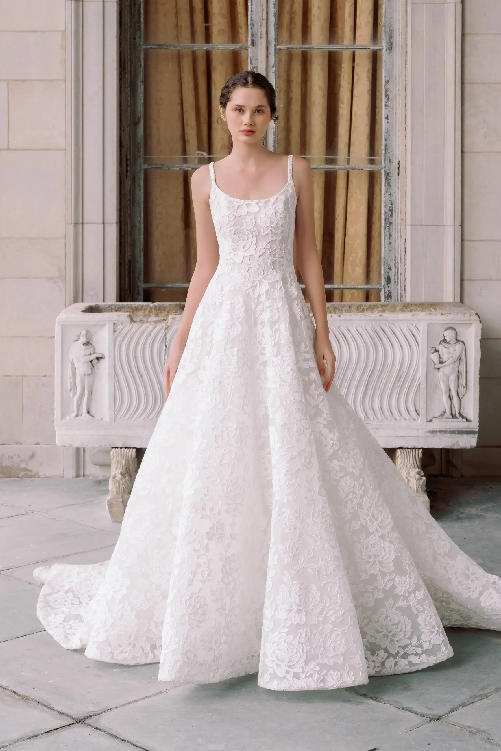 A model wearing a beautiful white lace wedding dress standing in front of an ornate building.